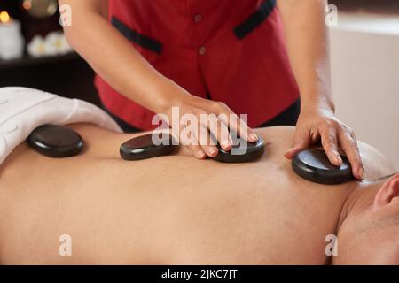 Nahaufnahme eines unverkennbaren Mannes, der während des Wochenendes in einem luxuriösen Spa-Salon eine Hot-Stone-Massage genießt Stockfoto