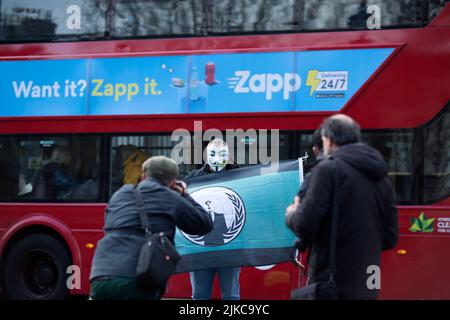 Eine Person, die eine Maske trägt, wird während eines „Cost of Living Crisis“-Protestes in der Nähe der Downing Street in London von Fotografen umgeben. Stockfoto