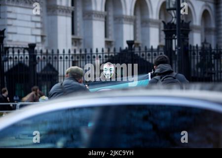 Eine Person, die eine Maske trägt, wird während eines „Cost of Living Crisis“-Protestes in der Nähe der Downing Street in London von Fotografen umgeben. Stockfoto