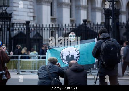 Eine Person, die eine Maske trägt, wird während eines „Cost of Living Crisis“-Protestes in der Nähe der Downing Street in London von Fotografen umgeben. Stockfoto