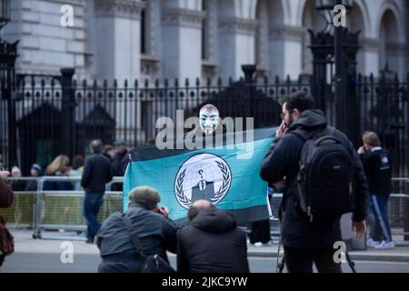 Eine Person, die eine Maske trägt, wird während eines „Cost of Living Crisis“-Protestes in der Nähe der Downing Street in London von Fotografen umgeben. Stockfoto