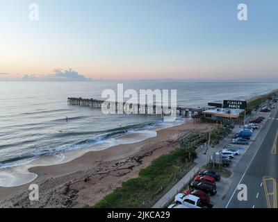 Eine Reihe von geparkten Autos auf der Straße neben einem schönen Sandstrand mit einem Pier Stockfoto