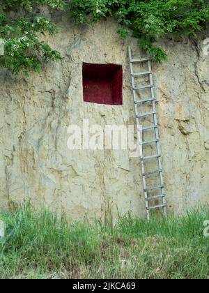 Eine vertikale Aufnahme einer hölzernen Leiter, die an einer Klippe mit einem quadratischen Loch lehnt Stockfoto