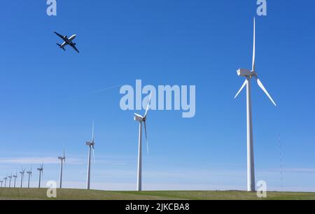 Flugzeug, das über einem Windturbinenpark fliegt. Erneuerbare Windenergie gegen den blauen Himmel. Stockfoto