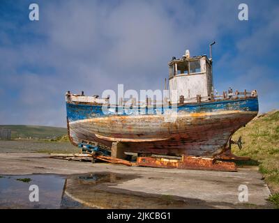 Ein altes, baufälliges Fischerboot aus Holz auf einem Parkplatz in Cumlewick, Scndwick, Shetland, Großbritannien. Aufgenommen an einem sonnigen Tag mit leichten Wolken. Stockfoto