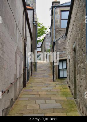 Ein enger, steiler Fußweg mit grünem Moos auf einigen Steinplatten zwischen Gebäuden in Lerwick, Shetland, Großbritannien. Ein Handlauf erscheint auf der linken Seite. Stockfoto