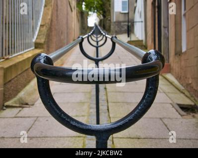 Ein doppelter Metallhandlauf führt einen steilen Gehweg mit Granitfelsen zwischen Gebäuden in Lerwick, Shetland, Großbritannien, hinauf. Stockfoto