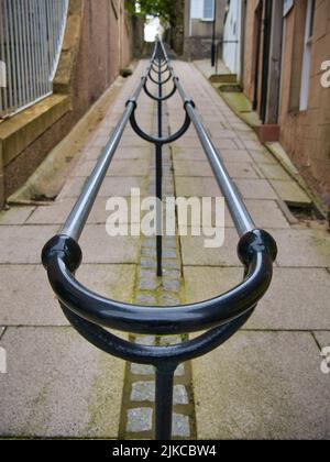 Ein doppelter Metallhandlauf führt einen steilen Gehweg mit Granitfelsen zwischen Gebäuden in Lerwick, Shetland, Großbritannien, hinauf. Stockfoto