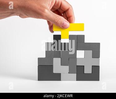 Hand setzen herausragende gelbe Element in Tetris Puzzle. Formationskonzept. Kreative einzigartige Idee. Logisches Spiel für die Entwicklung von Problemlösungsfähigkeiten. Hochwertige Fotos Stockfoto