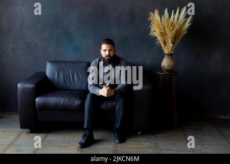Ein Mann mit schwarzem Bart sitzt auf einem Ledersofa. Geschäftsmann Stockfoto