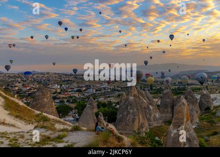 GOREME/TÜRKEI - 30. Juni 2022: Touristen beobachten das Schauspiel der Heißluftballons, die im Morgengrauen über ihnen fliegen. Stockfoto