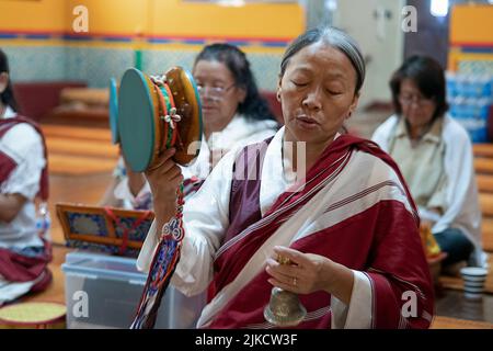 Ein frommer Nepalesischen Buddhistischen betende Frau im Tempel beim Klingeln einer Glocke & Drehen eines Damaru drum. In Elmhurst, Queens, New York City. Stockfoto