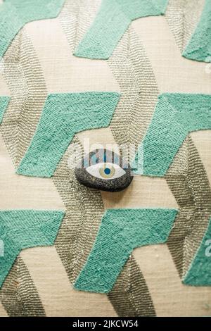 Böse Auge in weiß, blau, grün auf kleinen Felsen auf geometrischem Muster gemalt lassen in teal, silber, creme Stockfoto