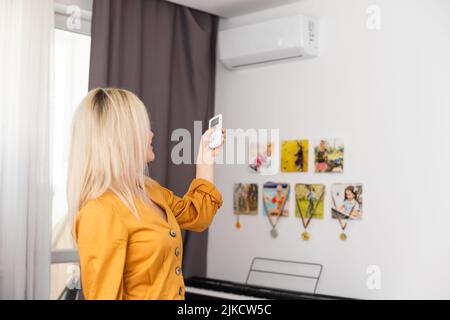 Frau mit Fernbedienung, die auf die Klimaanlage gerichtet ist Stockfoto