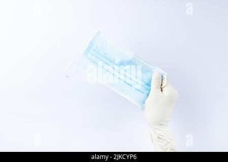 Die Hand einer Frau in einem weißen medizinischen Handschuh hält eine medizinische Maske. Auf weißem Hintergrund. Viel Platz Stockfoto