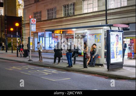 LONDON - 17. Mai 2022: Nachts warten Menschen an einer Londoner Bushaltestelle Stockfoto