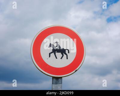 Verbotsschild für Pferde und Reiter. Dreieckiges Schild mit rotem Streifen und dunklem Bild auf hellem Hintergrund des Reiters auf dem Pferd. Stockfoto