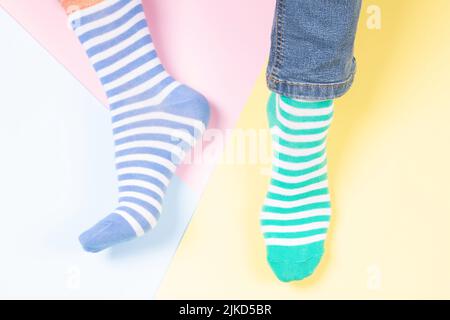 Lustige Füße in unpassenden Strippsocken auf buntem Hintergrund. Odd Socks Day, Anti-Mobbing Week, Down-Syndrom-Bewusstsein Konzept Stockfoto