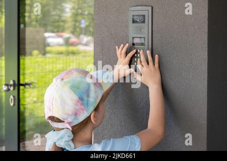 Kind im Grundschulalter, Mädchen, das ein Eingangstelefon benutzt, den Zugangscode allein im Freien eingibt, Wohnblock, Eingang zum Wohngebiet des Gebäudes Stockfoto