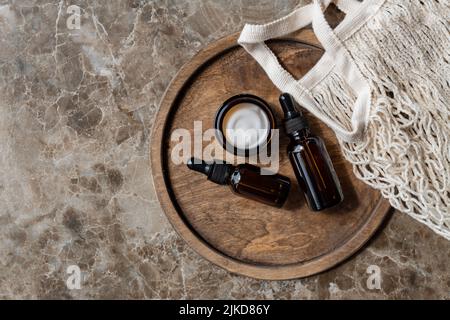 Gesichtscreme, Serum, ätherisches Öl in Glasflaschen und Mesh-Baumwollbeutel auf beigem Hintergrund. Flach liegend, Draufsicht. Set für Haut- und Körperpflege Stockfoto