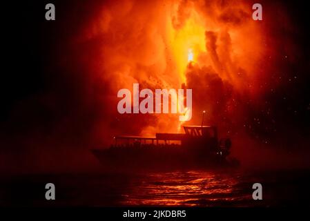 Ein Touristenboot schwebt nachts vor explodierender Lava und gibt den Menschen einen Blick auf die Mutter Natur in ihrer Wut. Stockfoto