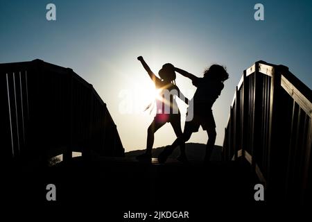 Junge und Mädchen Silhouetten tanzen auf einer Brücke gegen die Sonnenuntergangssonne Stockfoto