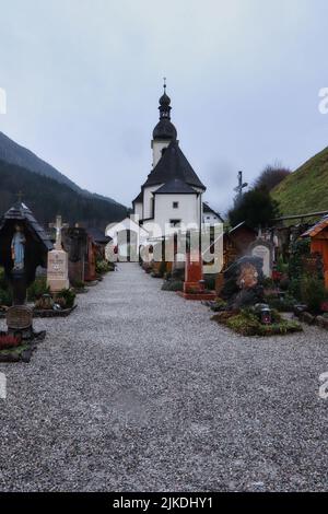 Ramsau, Deutschland - 29. November 2019: St. Sebastian Kirche hinter einem kleinen Friedhof an einem bewölkten, verschneiten Herbsttag in Ramsau, Deutschland. Stockfoto