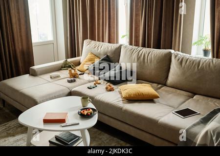 Teil des geräumigen Wohnzimmers in einer modernen Wohnung mit einem bequemen grauen Ledersofa mit Spielzeug und Kissen und einem kleinen Tisch, der davor steht Stockfoto