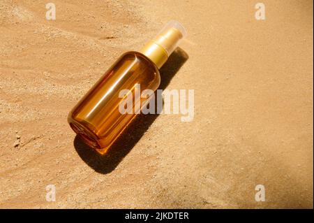 Dunkle Glasflasche ohne Marke mit SPF-Öl oder Sonnencreme auf Sandstrand-Hintergrund. Sommerliches Kosmetikkonzept. Stockfoto