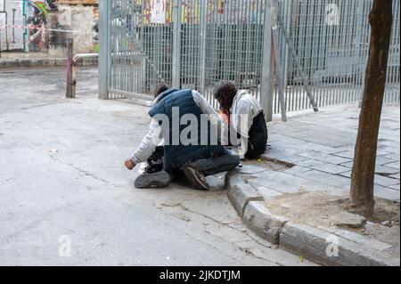 ATHEN, GRIECHENLAND - 14. MAI 2022: Ein Obdachloser schläft auf einem Bürgersteig in der Innenstadt von Athen. Touristen kommen vorbei. Stockfoto