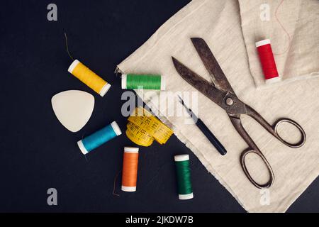 Alte Schere, Spulen aus farbigem Garn, Zentimeter- und Schneiderkreide, flaches Lay, Konzept der Nähkleidung Stockfoto