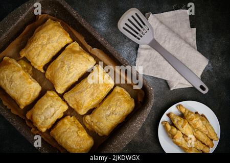 Heißer Blätterteig und Käsepatties liegen in einem antihaftbeschichteten Backblech, flach liegend Stockfoto