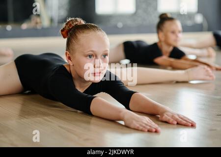 Flexibles Mädchen, das während der Wiederholung oder des Ballettuntermales die Arme in der Garnhaltung nach vorne blickt und die Arme ausdehnt Stockfoto