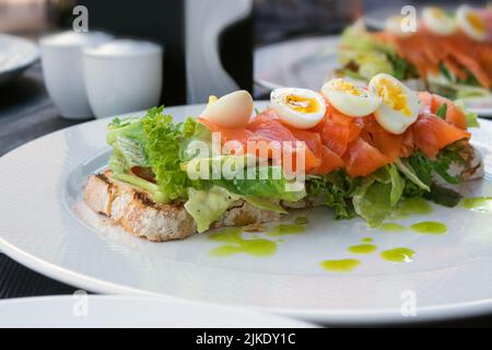 Großes, leckeres Sandwich mit Lachs, Wachteleiern und Gemüse. Mittagessen in einem Restaurant. Richtige Ernährung. Stockfoto