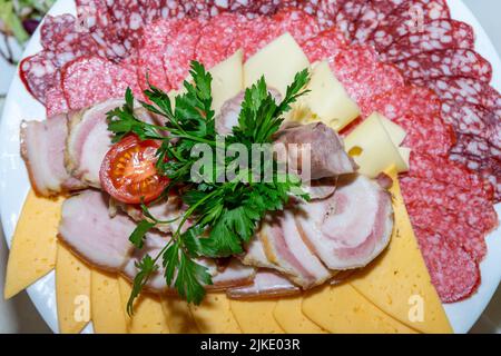 Ein Teller mit kalten Vorspeisen mit verschiedenen Würstchen, Fleisch und Käse. Grünpflanzen und Tomaten Stockfoto