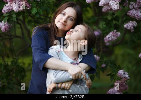 Mutter und Tochter vor dem Hintergrund eines blühenden Fliederbusches. Stockfoto