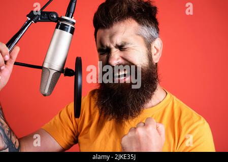 Emotionaler männlicher Sänger, der im Kondensatormikrofon singt. Professioneller Sänger im Studio. Musik. Stockfoto