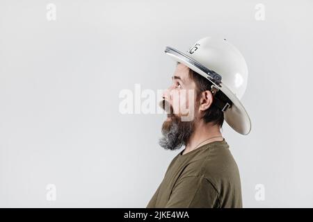 Feuerwehrmann mit offenem Mund. Verrückter bärtiger Mann in einem Feuerwehrhelm. Profilansicht. Stockfoto