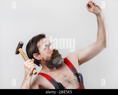 Arbeiter hämmert einen Nagel mit einem Hammer. Bärtiger Mann mit Hammer. Stockfoto