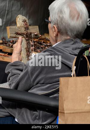 Eine ältere Frau im Rollstuhl erwägt, beim jährlichen Open-Air-Kunstfestival Spanish Market in Santa Fe, New Mexico, einen Kauf zu tätigen. Stockfoto