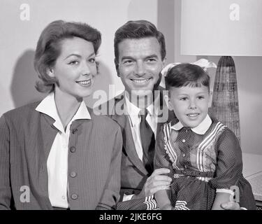 1950S 1960S PORTRÄT LÄCHELND FAMILIE MUTTER VATER UND EINE TOCHTER SITZEN AUF DAD’S SCHOSS ALLE BLICK AUS DER KAMERA LÄCHELND - J1022 HAR001 HARS NOSTALGIE ALTE MODE 1 JUVENILE STIL FREUDE FRAUEN VERHEIRATET EHEGATTEN EHEMÄNNER DAMEN TÖCHTER PERSONEN MÄNNER VÄTER B&W PARTNER ANZUG UND KRAWATTE FRÖHLICH UND VÄTER LÄCHELT KERNFAMILIE FRÖHLICH JUVENILE MÜTTER FRAUEN SCHWARZ-WEISS KAUKASISCHEN ETHNIE HAR001 ALTMODISCH Stockfoto