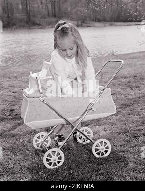 1960S KLEINES BLONDES MÄDCHEN IM HINTERHOF, DAS IN EINEM SPIELZEUGWAGEN ZU IHRER PUPPE TENDIERT - J12172 HAR001 HARS KOPIE RAUM HALBE LÄNGE STREAM CARING B & W WAGEN MÜTTERLICHE TRÄUME GLÜCK HIGH ANGLE WEIBLICHE PHANTASIE ROLLE SPIELEN BABY BUGGY GESCHLECHTSWACHSTUM JUGENDLICHE BABYWAGEN SCHWARZ UND WEISS KAUKASISCHE ETHNIE HAR001 ALTMODISCHE PFLEGE Stockfoto