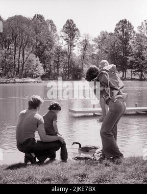 1970S RÜCKANSICHT EINER VIERKÖPFIGEN FAMILIE AM SEE MIT ENTEN, KANADAGÄNSE, JUNGE AUF DEM SCHOSS DER MUTTER, DIE DAS BABY TRÄGT IN BACK PACK - J14159 HAR001 HARS 4 JEANS MÜTTER ALTE ZEIT NOSTALGIE BRUDER ALTE MODE 1 JUGENDLICH STIL KANADA JUNGE ERWACHSENE BAUMWOLLE SÖHNE FAMILIEN VÖGEL FRAUEN BRÜDER PACK DAMEN PERSONEN MÄNNCHEN ENTEN DENIM VÄTER B&W LAP LAKESIDE FLÜGEL VÄTER RÜCKANSICHT GESCHWISTER VON HINTEN WIRBELTIEREN WARMBLÜTIG RÜCKANSICHT BLAUE JEANS GEFIEDERTE GÄNSE INFORMELLE JUGENDLICHE MÜTTER TWILL GEFLÜGELTEN JUNGEN ERWACHSENEN MANN JUNGER ERWACHSENER FRAU BABY MÄDCHEN ZWEIBEINER SCHWARZ UND WEISS BEILÄUFIGE KAUKASISCHE ETHNIE EIABLAGE HAR001 Stockfoto