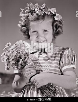 1940S KLEINES MÄDCHEN MIT EINEM STRAUSS GÄNSEBLÜMCHEN UND EINER KRONE VON GÄNSEBLÜMCHEN IM HAAR UND LÄCHELND IN EINEM GESTREIFTEN KLEID BLICK IN DIE KAMERA - J1905 HAR001 HARS SIEGREICHE FLORALE LÄNDLICHE GESUNDHEIT NATUR KOPIEREN RAUM GIRLANDE HALBE LÄNGE INSPIRATION VERTRAUEN B&W DAISY SOMMERZEIT BLICKKONTAKT GÄNSEBLÜMCHEN TRÄUME GLÜCK FRÖHLICH UND STOLZ LÄCHELT FRÖHLICH STILVOLL ANGENEHM ANGENEHM REIZEND WACHSTUM JUGENDLICHE LIEBENSWERT ANGENEHME JAHRESZEIT LIEBENSWERT ANSPRECHEND SCHWARZ UND WEISS KAUKASISCHEN ETHNIZITÄT HAR001 ALTMODISCH Stockfoto