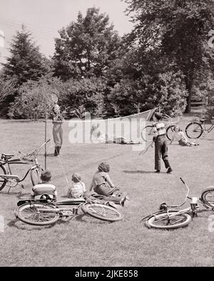 1950S GRUPPEN VON KINDERN IN DER NACHBARSCHAFT SPIELEN BADMINTON IM PARK 2 IM NET UND 6 KINDER BEOBACHTEN FAHRRÄDER PARK HERUM AUF GRAS - J4958 HAR001 HARS TEAMWORK BADMINTON ATHLET FREUDE LIFESTYLE FRAUEN RADFAHREN GESUNDHEIT 6 KOPIEREN RAUM FREUNDSCHAFT VOLLE LÄNGE HALBLÄNGE PERSONEN MÄNNER TEENAGER MÄDCHEN TEENAGER JUNGE SPORTLICHE FAHRRÄDER ZAHLEN TRANSPORT S & W FAHRRÄDER AKTIVITÄT GLÜCK KÖRPERLICHE NACHBARSCHAFT HIGH-WINKEL ABENTEUER STÄRKE UND PARKS ERHOLUNG FLEXIBILITÄT FREUNDLICH MUSKELN TEENAGED ZUSAMMENARBEIT PRE-TEEN PRE-TEEN JUNGE PRE-TEEN MÄDCHEN ZWEISAMKEIT SCHWARZ UND WEISS KAUKASISCHE ETHNIE HAR001 ALT MODISCH Stockfoto