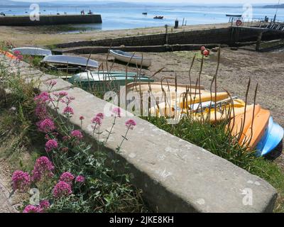 Am Strand von Findhorn Bay, einem wichtigen Segel- und Wassersportziel im Nordosten Schottlands, stehen bunte, umgedrehte Kanus und kleine Boote. Stockfoto