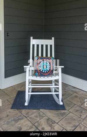 Eine gestempelte Betonfront Veranda mit einem weißen Schaukelstuhl mit einem bunten Kissen Stockfoto