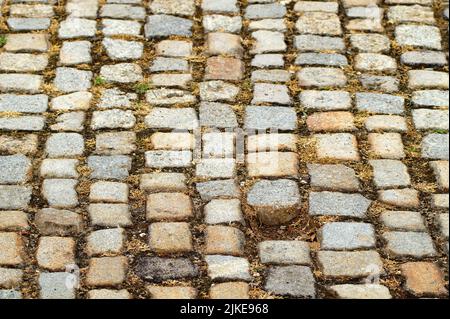 Pflastersteine aus rechteckigen und quadratischen Steinen in verschiedenen Farben und Größen. Ein Stein fehlt an der Kopfsteinpflasterstraße. Stockfoto