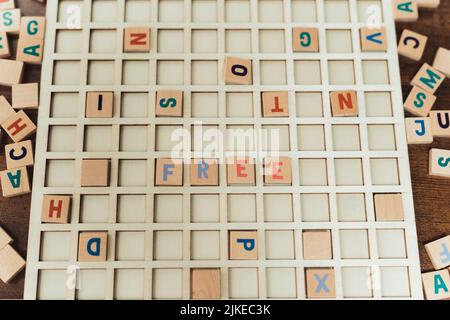 Werbekonzept. Verschiedene bunte Buchstaben auf einem Brett, zwei blaue quadratische Holzbuchstaben und zwei orangefarbene Buchstaben schaffen Wort FREI. Hochwertige Fotos Stockfoto