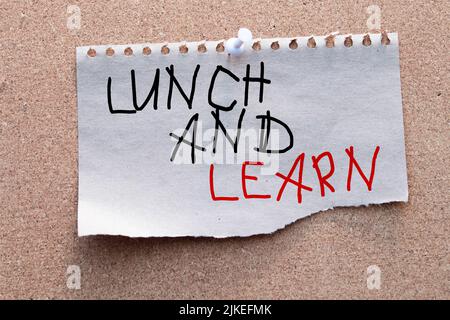 Lunch and Learn, Ein spiralförmiges Notizpad, das die Worte Lunch and Learn über einen verzweifelten Holzhintergrund hat. Stockfoto